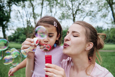 Daughter and mother blowing bubbles at park - ASGF00692