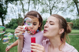 Tochter und Mutter beim Blasen von Seifenblasen im Park - ASGF00692