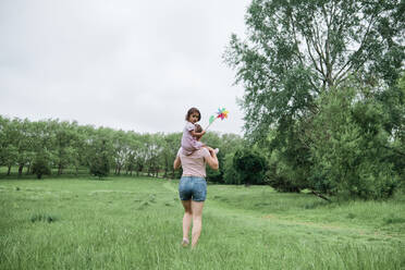 Mother carrying daughter on shoulders while walking in park - ASGF00703