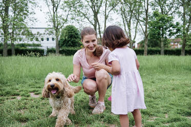 Mother and daughter playing with dog at park - ASGF00705