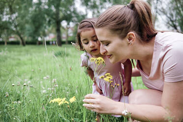 Mutter und Tochter riechen im Park an Blumen - ASGF00706