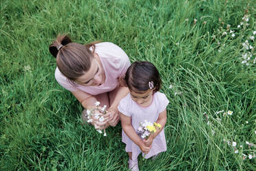 Mother and daughter holding flowers on grass at park - ASGF00709