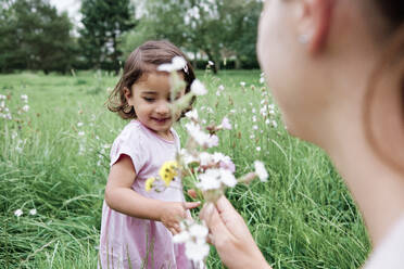 Cute girl with mother holding flowers on grass in park - ASGF00710