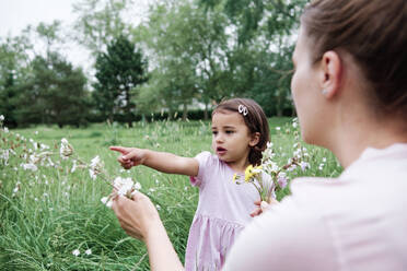 Mother holding flowers while daughter pointing at park - ASGF00712