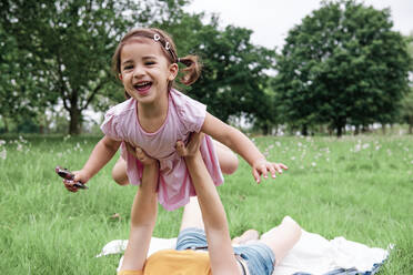 Woman playing with daughter while lying on grass in park - ASGF00719