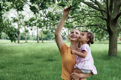 Mother showing leaves to daughter at park - ASGF00727