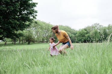 Mother and daughter running on grass in park - ASGF00732