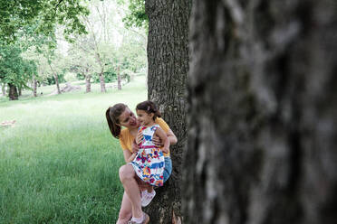Mutter und Tochter lehnen sich im Park an einen Baumstamm - ASGF00734