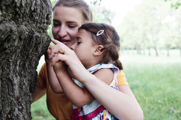Mother and daughter touching tree trunk at park - ASGF00737