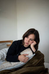 Woman sitting in bed under blanket looking deep in thought - CAVF94312