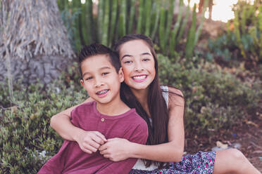 Older sister hugging young brother by a cactus garden - CAVF94316