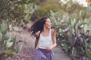 Gemischtrassiges Mädchen, das mit fliegenden langen Haaren auf einem Kaktuspfad läuft. - CAVF94325