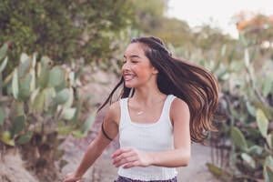 Gemischtrassiges Mädchen, das mit fliegenden langen Haaren auf einem Kaktuspfad läuft. - CAVF94327