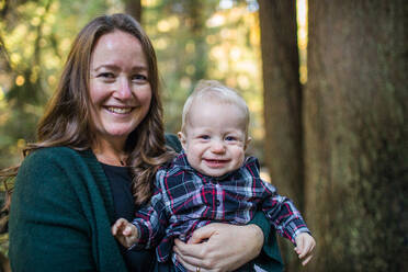 Porträt einer Mutter und eines kleinen Sohnes, die in einem Wald lächeln. - CAVF94348