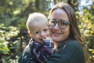 Porträt einer Mutter im Freien, die ihren einjährigen Sohn im Arm hält. - CAVF94356