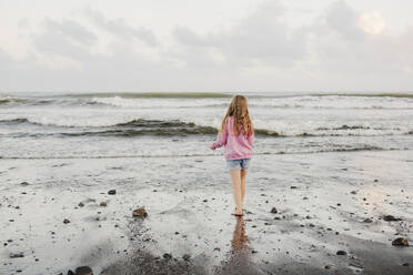 Young girl standing at the waters edge at the beach - CAVF94364