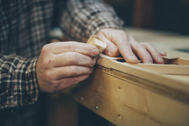 A Caucasian, middle aged man works on a small piece of a wooden airplane in his garage. - CAVF94381