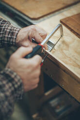 Ein kaukasischer Mann mittleren Alters arbeitet in seiner Garage an einem kleinen Teil eines Holzflugzeugs. - CAVF94382