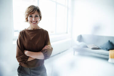 Smiling businesswoman with arms crossed standing in office - JOSEF04940