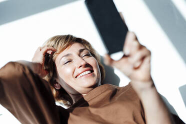 Smiling businesswoman using smart phone while lying on floor in office - JOSEF04951