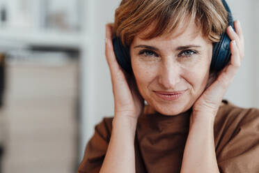 Businesswoman smiling while holding wireless headphones in office - JOSEF04977