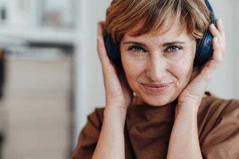 Geschäftsfrau lächelt, während sie drahtlose Kopfhörer im Büro hält - JOSEF04977