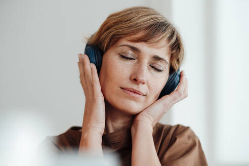 Weibliche Fachkraft mit geschlossenen Augen hört Musik über Kopfhörer im Büro - JOSEF04978