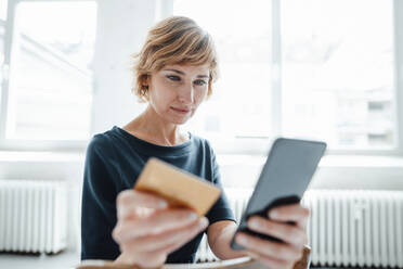 Businesswoman holding credit card while using mobile phone in office - JOSEF05008