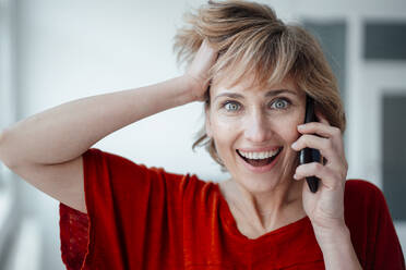 Businesswoman with hand in hair talking on mobile phone in office - JOSEF05019