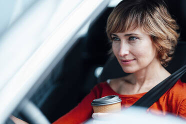 Businesswoman holding disposable cup while driving car - JOSEF05020