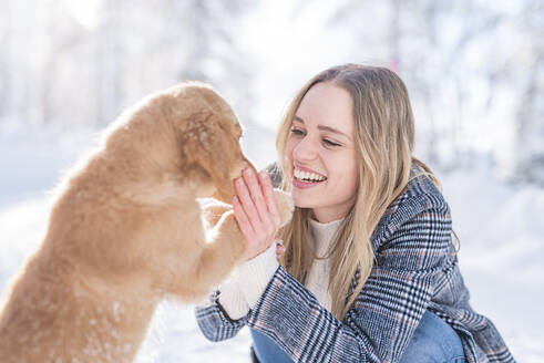 Fröhliche junge Frau streichelt Hund im Winter - MEF00108