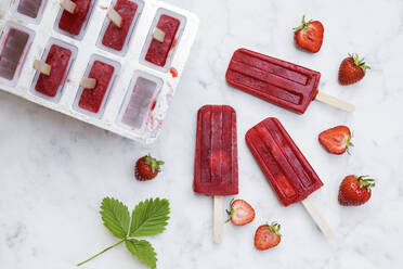 Homemade strawberry popsicles lying on marble surface - GWF07051