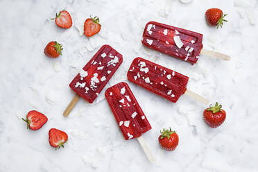 Homemade strawberry popsicles lying on marble surface - GWF07052