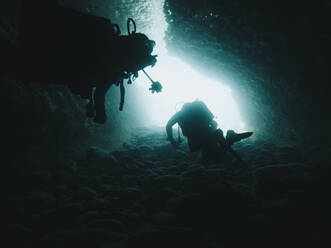 Young scuba divers swimming under cave in sea - RSGF00743
