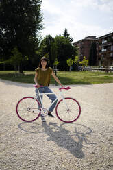 Woman with bicycle standing on footpath during sunny day - GIOF13024