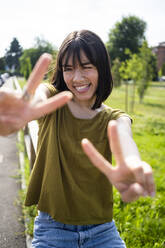 Woman showing peace sign while sitting on fence - GIOF13025