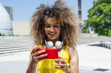 Glückliche junge Frau, die an einem sonnigen Tag ein Video über ihr Mobiltelefon ansieht - PGF00627