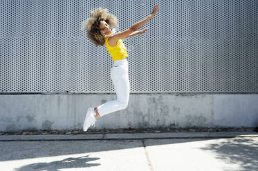 Excited young woman jumping on footpath during sunny day - PGF00638