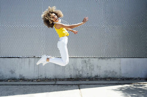 Glückliche junge Frau, die an einem sonnigen Tag auf dem Fußweg springt - PGF00639