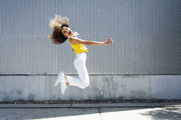 Happy young woman laughing while jumping on footpath - PGF00640