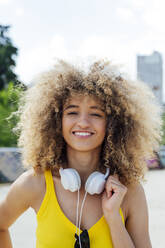 Lächelnde junge Frau mit lockigem Haar und Kopfhörern - PGF00645