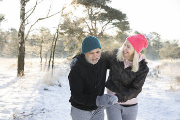 Cheerful senior couple holding hands while walking on snow - FVDF00318