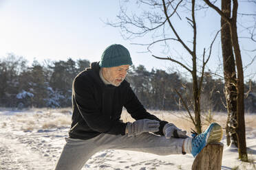 Älterer Mann streckt sein Bein beim Sport im Winter - FVDF00321