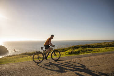 Älterer männlicher Sportler, der bei Sonnenuntergang auf der Straße Rad fährt - UUF23735