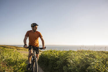 Smiling mature sportsman cycling amidst green grass - UUF23737