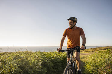 Mature sportsman riding electric mountain bike at sunset - UUF23738