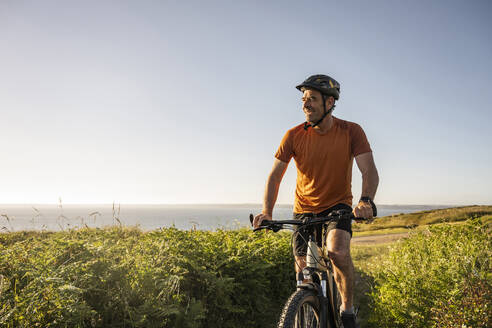 Mature sportsman riding electric mountain bike at sunset - UUF23738