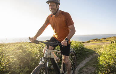 Happy sportsman cycling amidst green plants at sunset - UUF23739