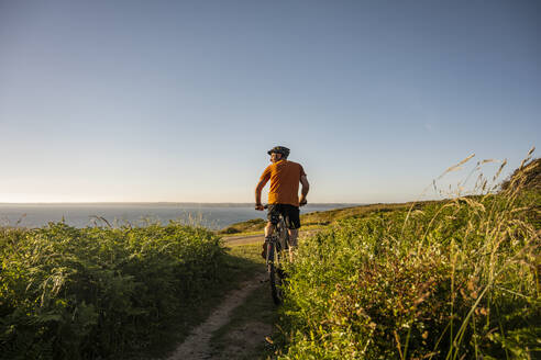 Mature male athlete riding electric mountain bike amidst plants at sunset - UUF23742