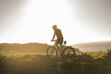 Älterer männlicher Sportler fährt Mountainbike bei Sonnenuntergang - UUF23745